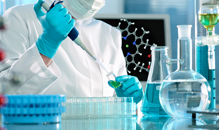 Scientist surrounded by glassware in a laboratory using a pipette