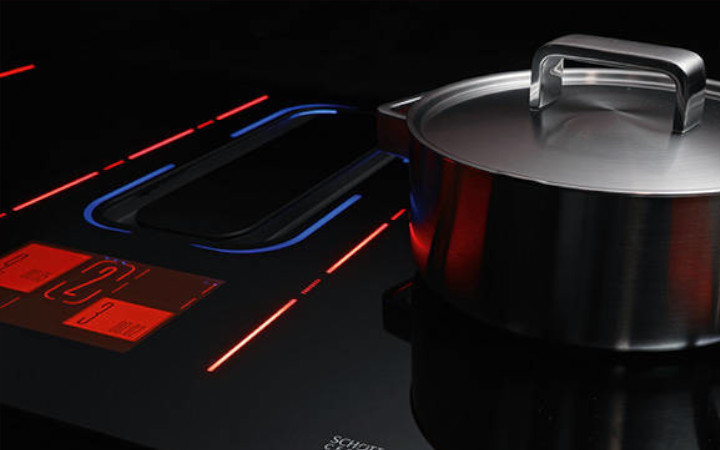 Cooking pan next to a dark glass-ceramic cooktop lit up with red and blue light