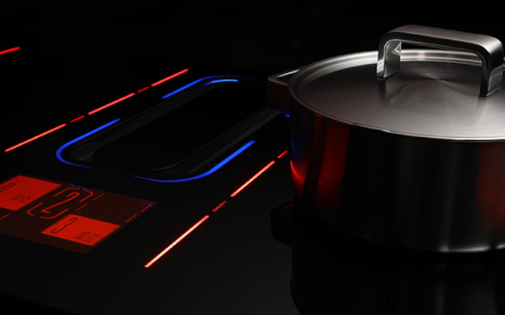 Cooking pan next to a dark glass-ceramic cooktop lit up with red and blue light