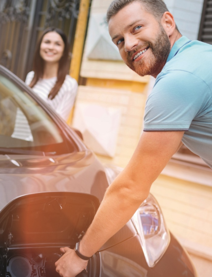Man charging an electric vehicle with woman looking on