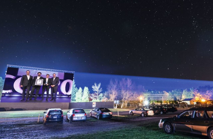 Outdoor screen at a drive-in with digital projection of an image of four men accepting award